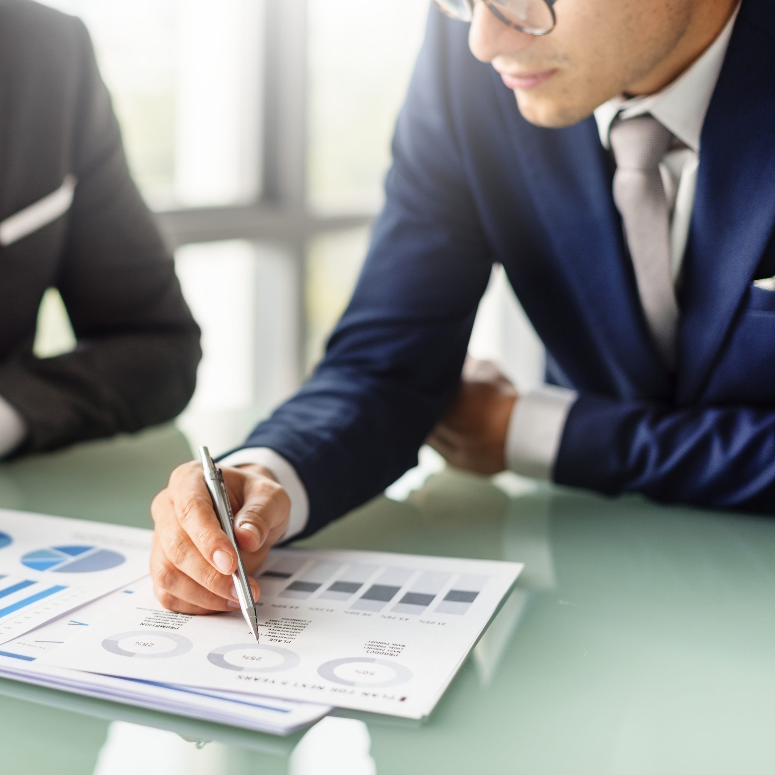 Two colleagues in suits reviewing printed charts across a table.