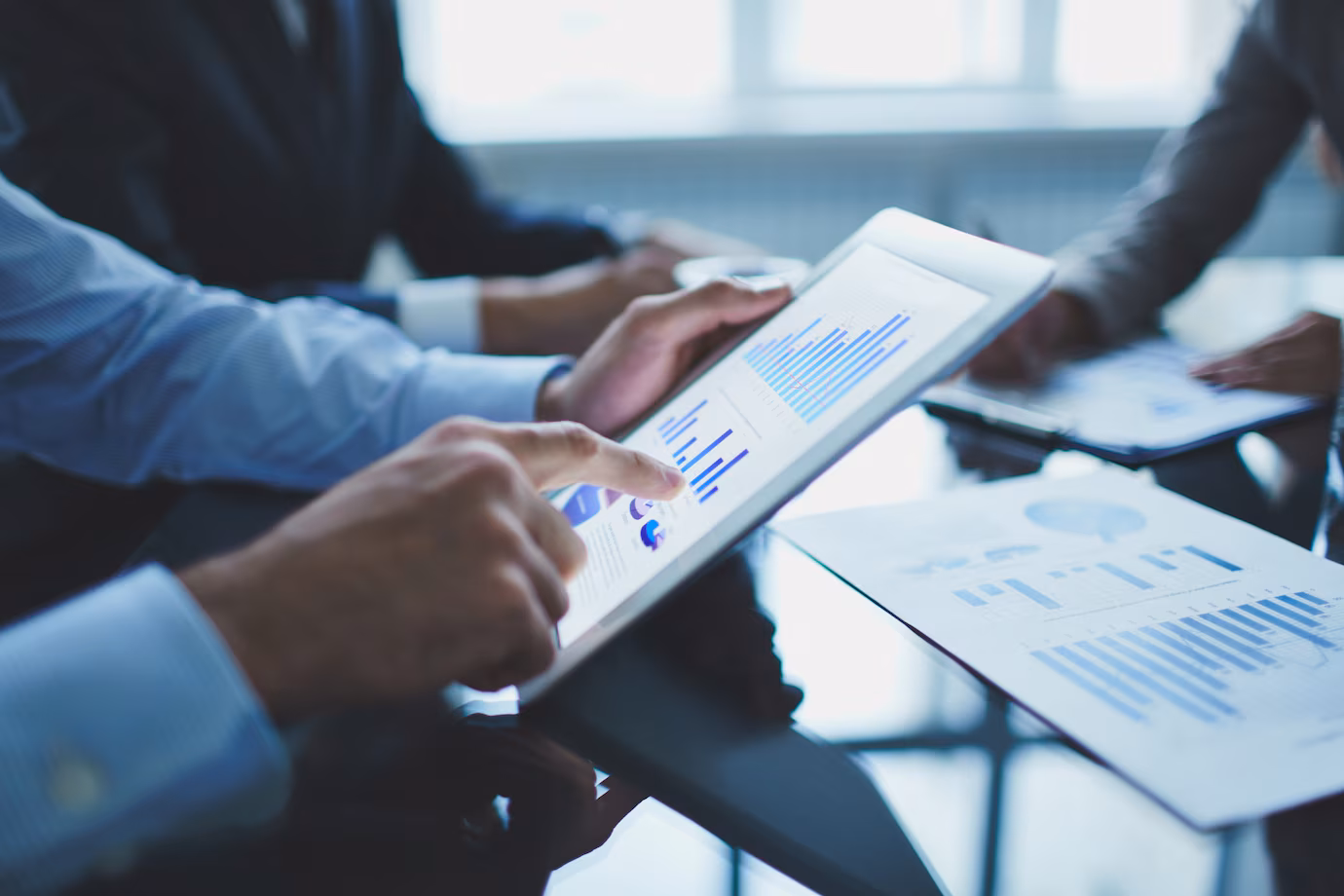 Hands using a tablet over printed charts during a meeting.