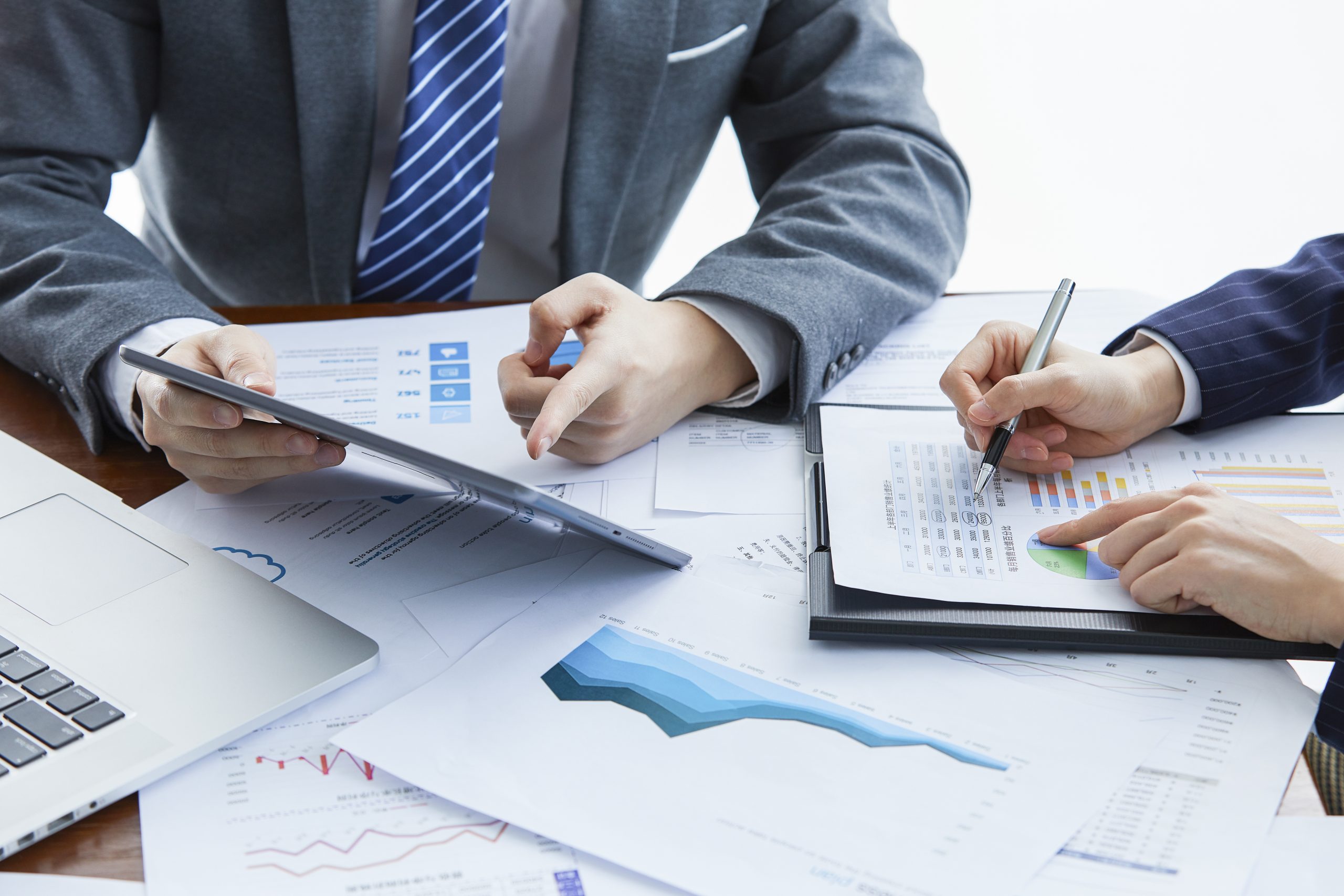 Colleagues in suits working across printed charts and a laptop at a meeting table.