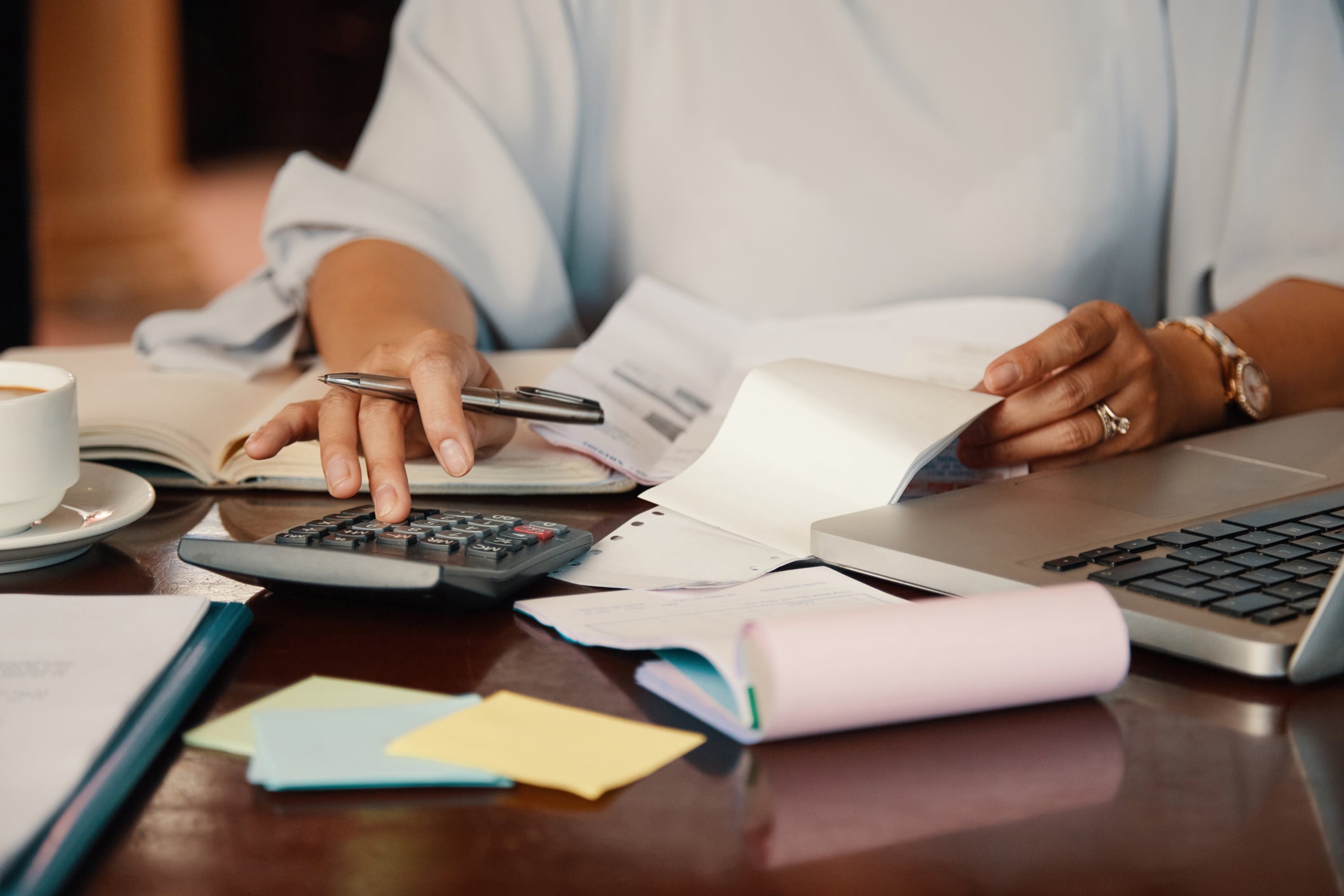 Hands at a calculator with bills and a laptop on a desk.