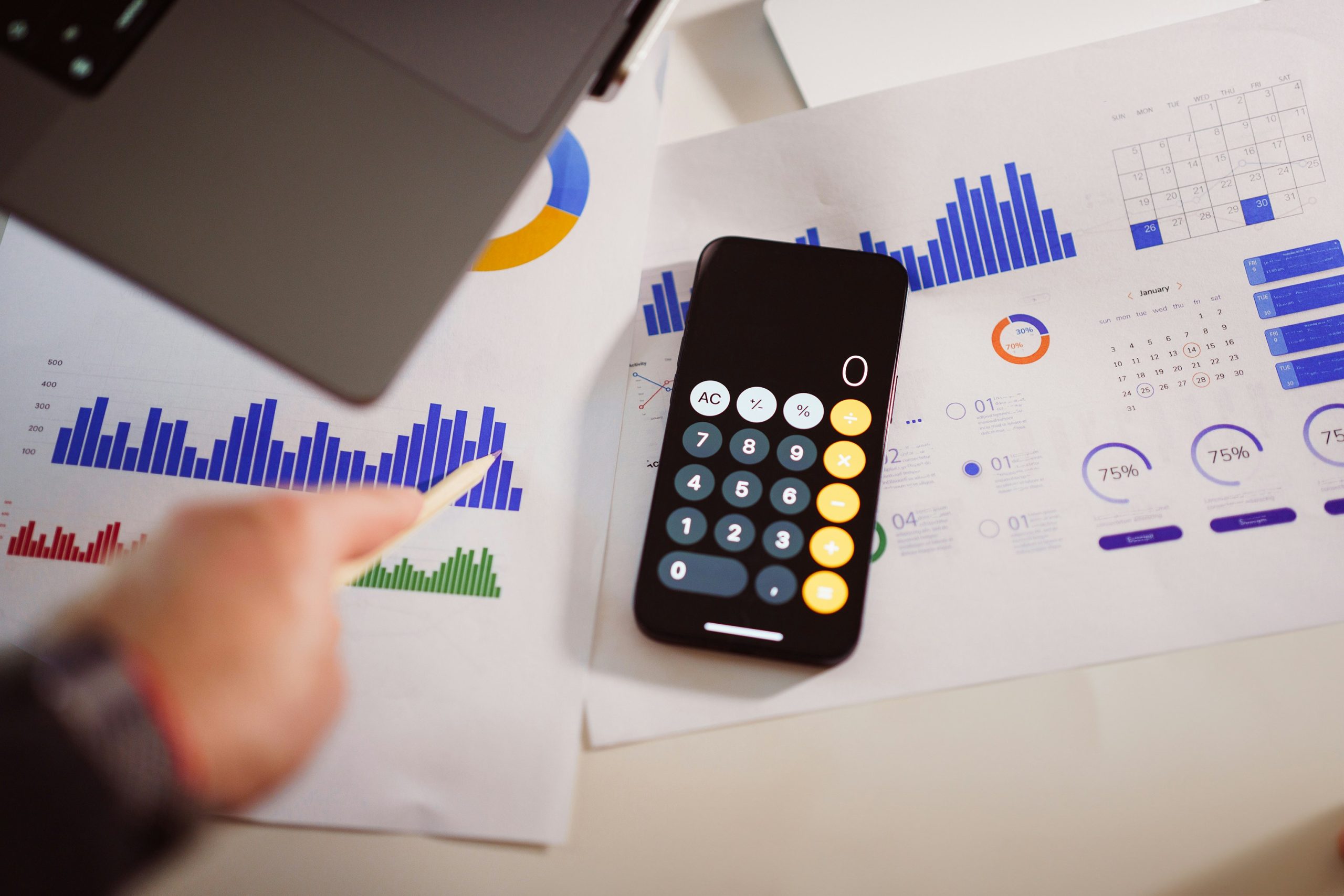 A calculator and phone on a desk covered with printed charts.