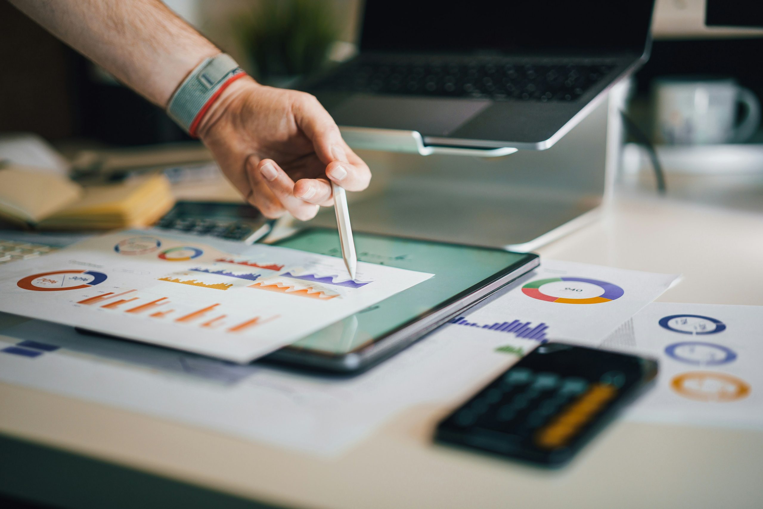 A hand marking up printed charts beside a laptop.