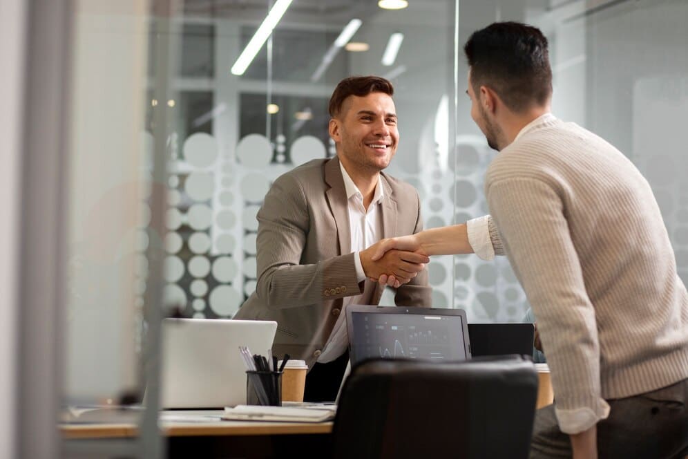 Two men shaking hands and smiling in an office.