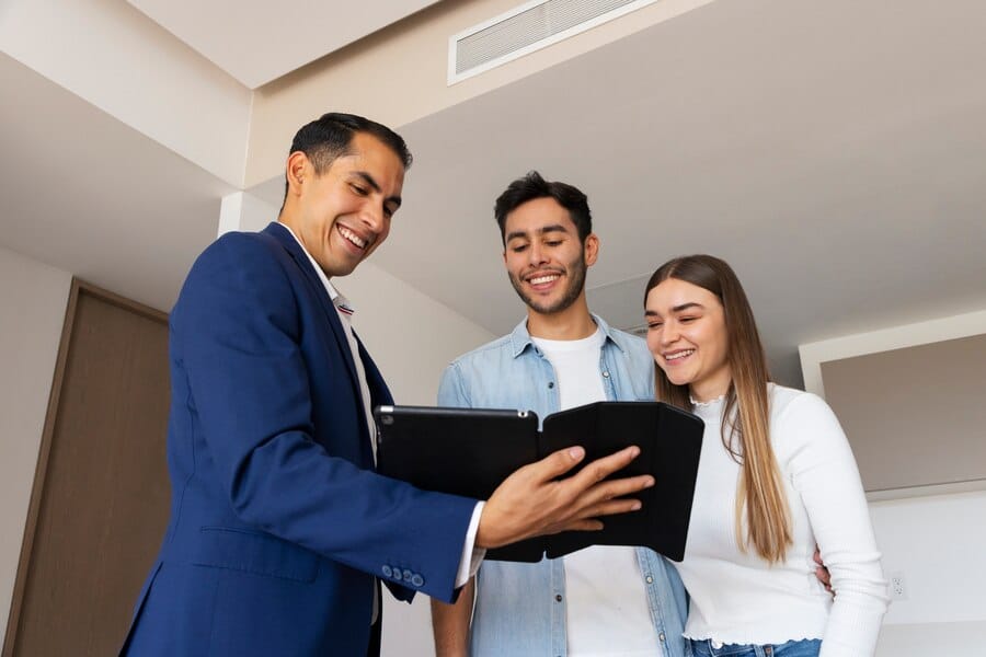 An adviser shows a folder to a young couple in a bright hallway.