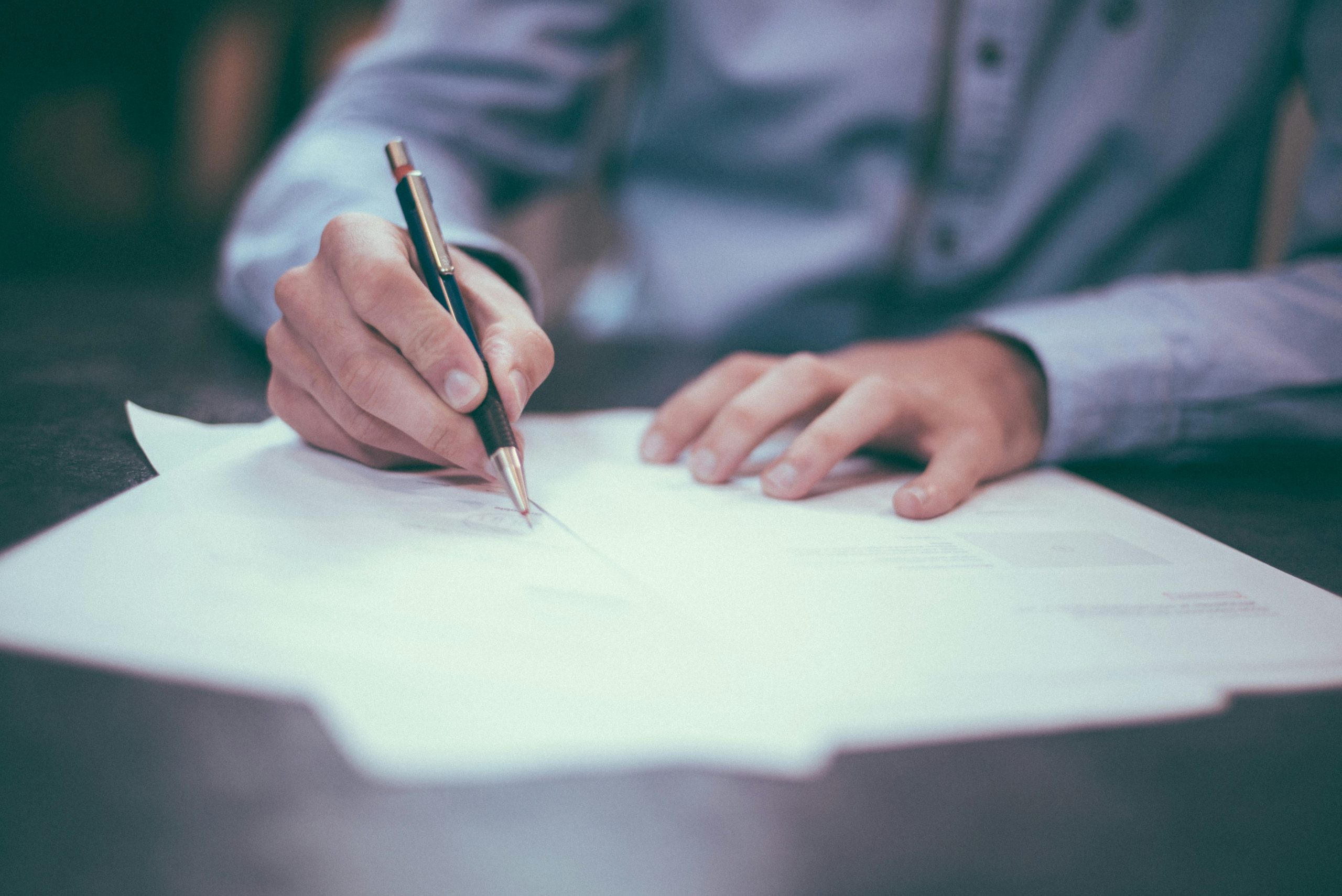 A hand signing a document with a pencil.