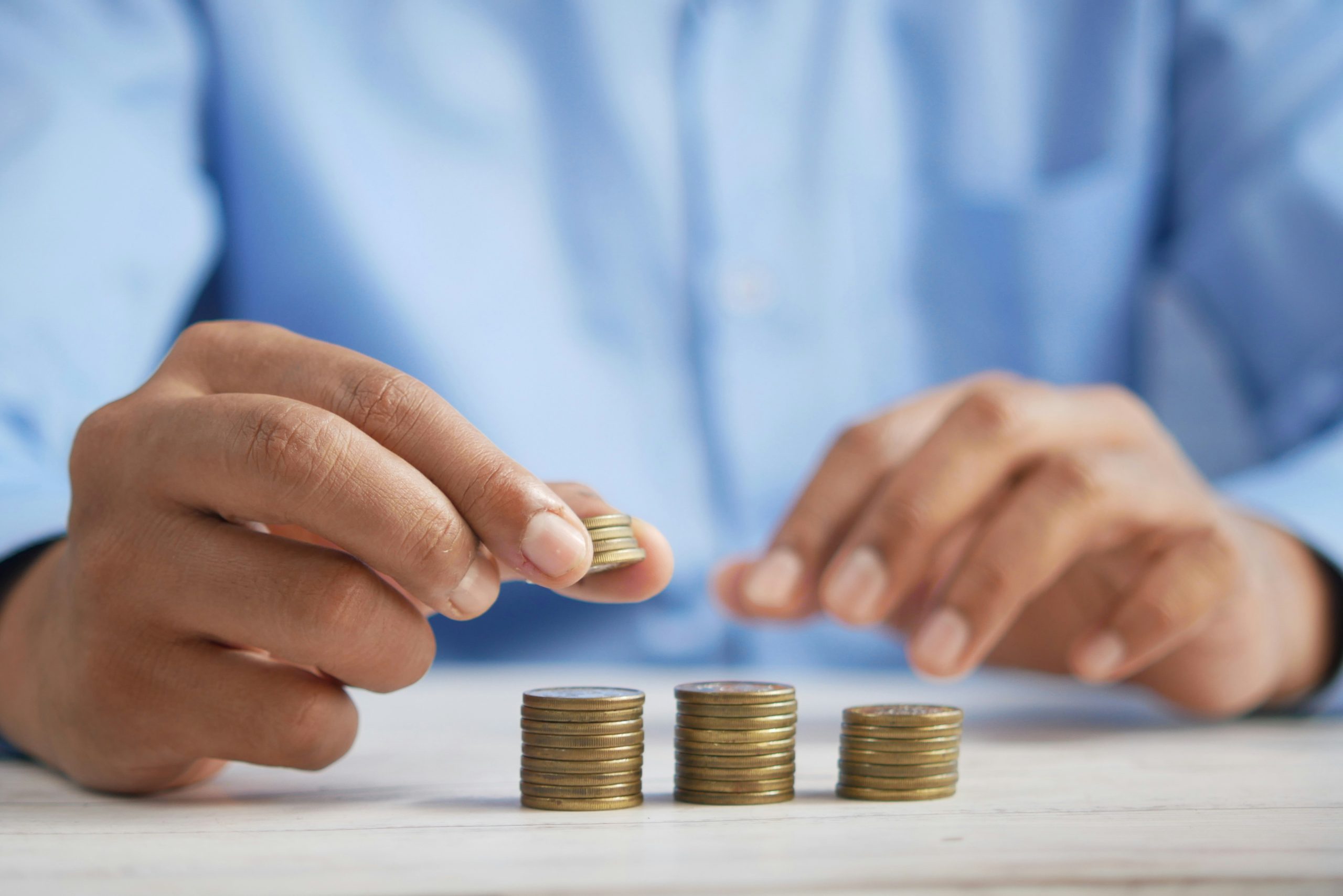 Hands stacking coins into rising columns on a desk.